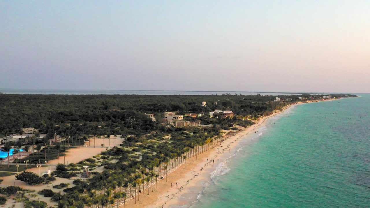 A serene aerial shot of the Cancun coastline during dusk, showcasing lush greenery, soft beach sands, and calm turquoise waters extending into the horizon.