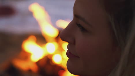 woman sitting by camp fire on beach as sun sets behind her