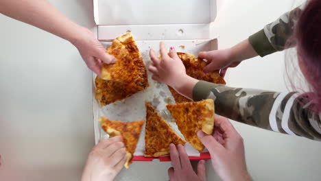 hands grabbing slices of pizza from a pizza box