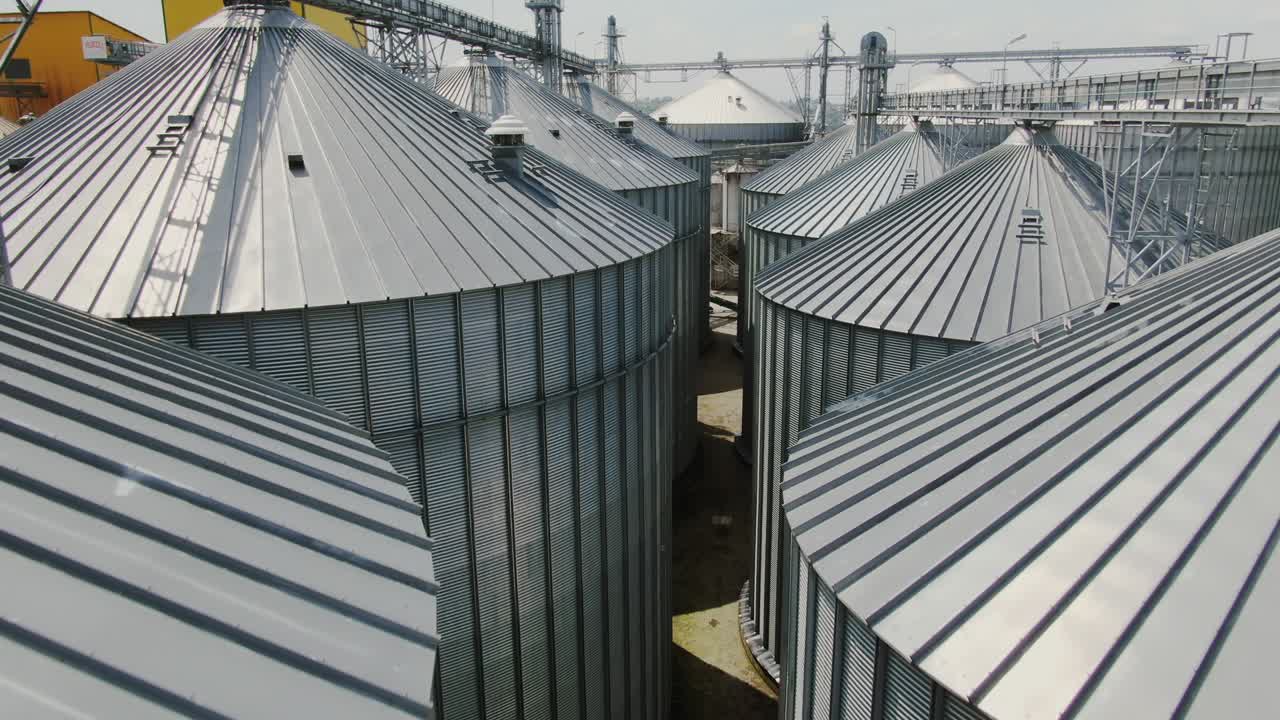 volando lentamente más allá de las cimas de los silos cónicos industriales de metal de pie cerca el uno del otro sin personas a la vista