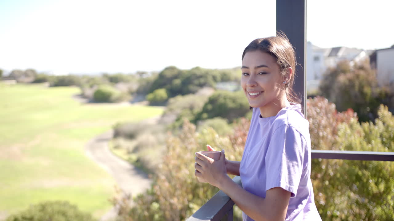 Smiling woman holding coffee cup, enjoying view from balcony at home, copy space
