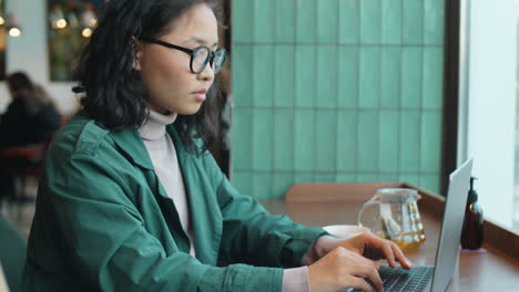 asian woman working on laptop and drinking tea in cafe