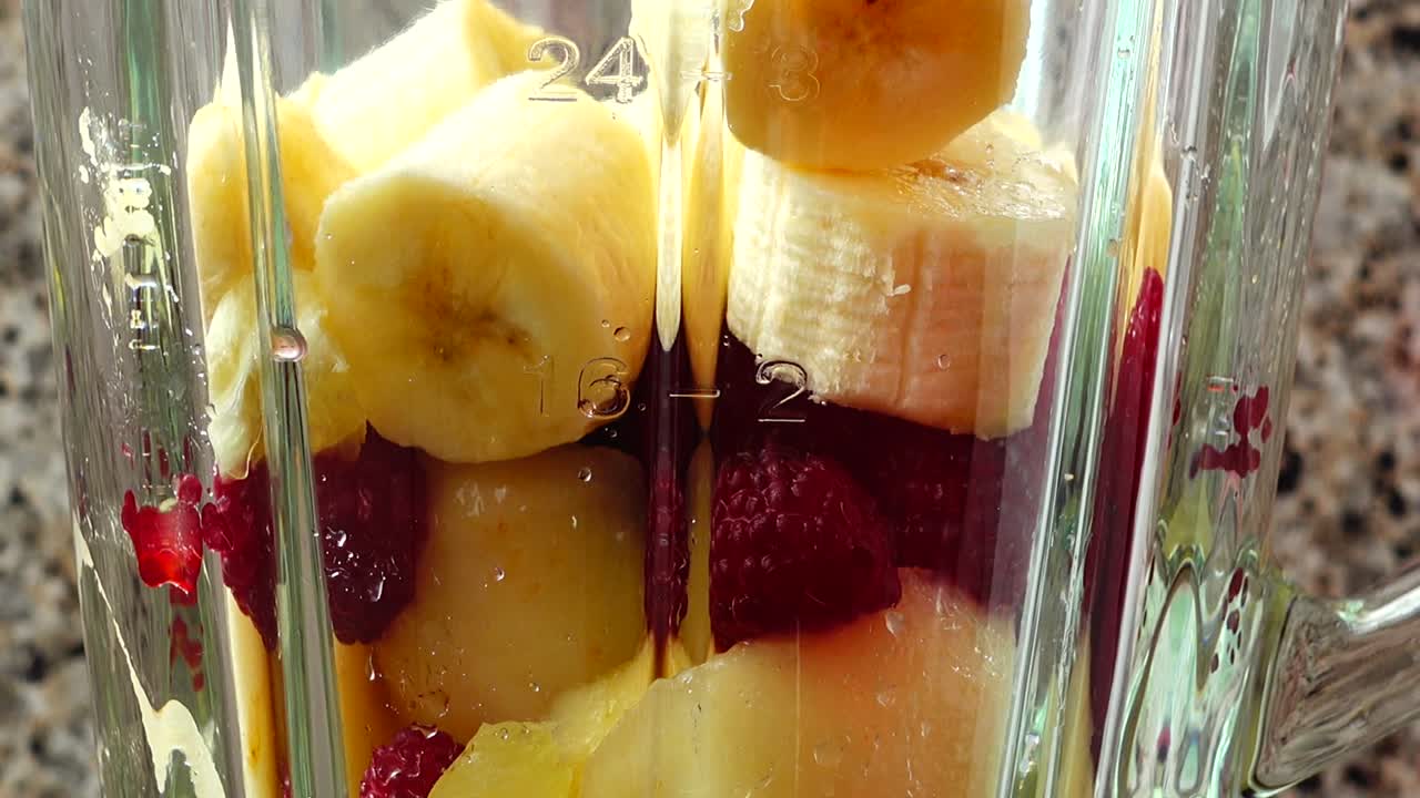 Fyller blenderen med biter av pære, bringebær og bananer