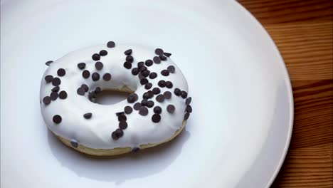 close-up shot of glazed white donut with chocolate chips spinning around and bitten on wooden table background.