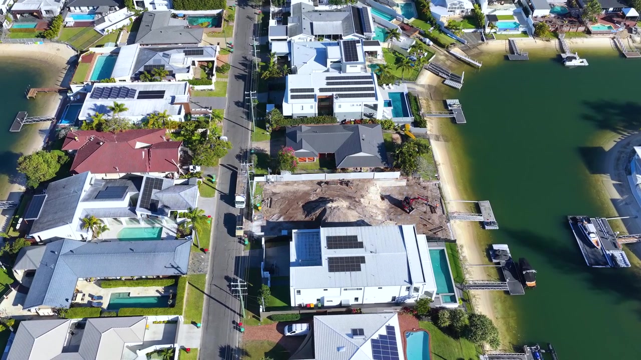 High-angle drone shot of luxury homes and a construction site along Gold Coast canals.