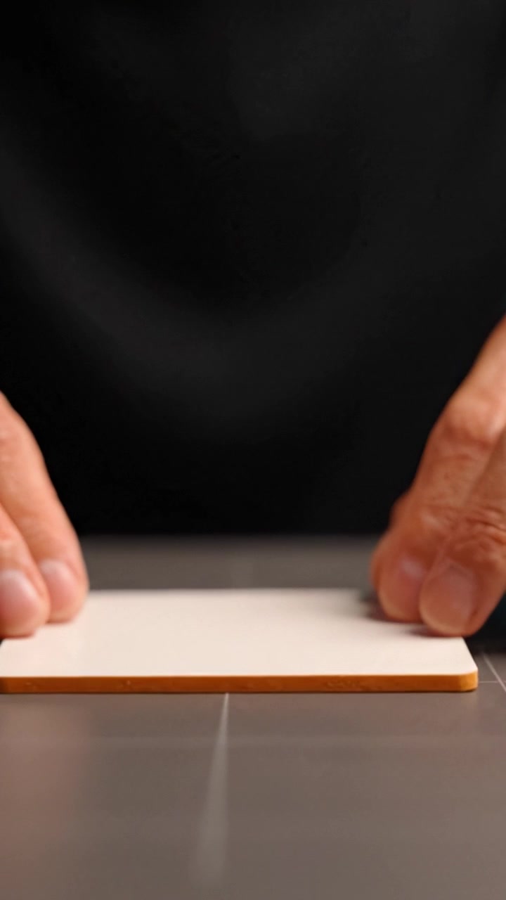 Hände halten eine Karte über einer Tischoberfläche, fokussierte Details und minimalistische Komposition in einer kreativen Arbeitsumgebung zeigend.