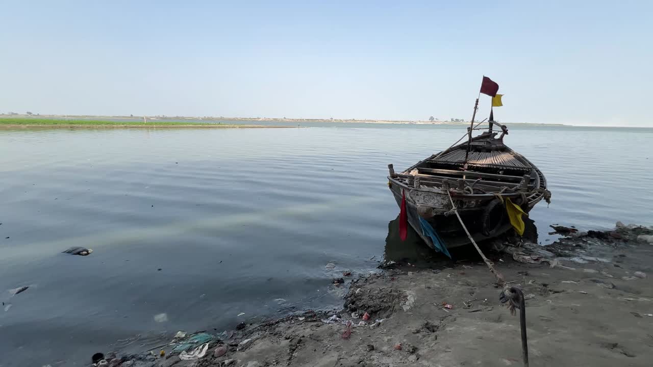 Wooden boat anchored to muddy shore during daytime in Ganga, Patna. Blue clear sky.