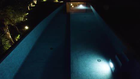 aerial tilting shot showing a luxury villa interior and blue private pool at night