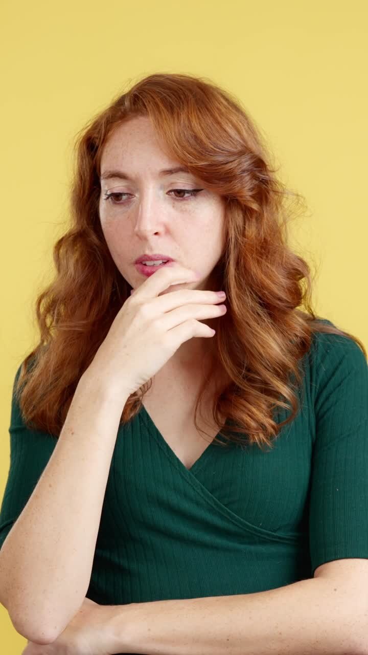 A red-haired woman looks sad and distressed against a yellow background
