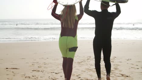 Back-view-of-surfers-walking-on-sandy-beach