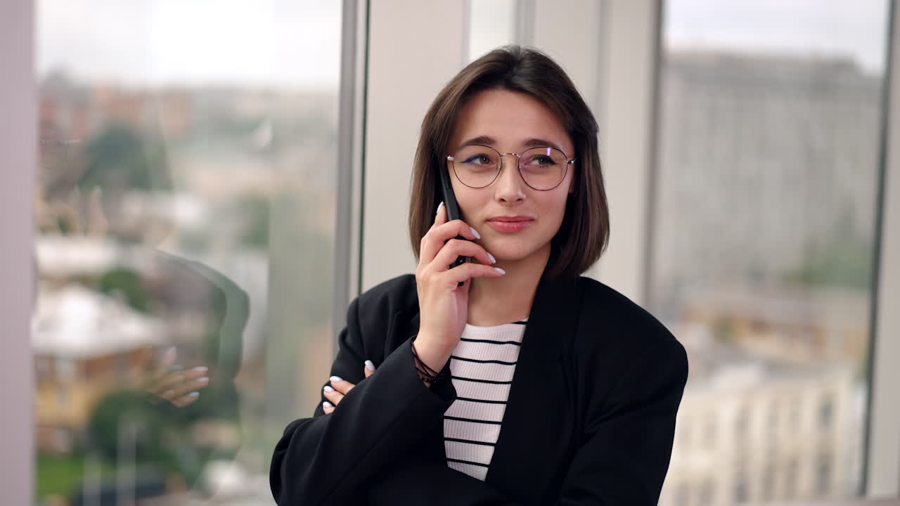 Smiling Caucasian brunette in glasses talks on the phone. Portrait of a business lady having business conversation. Close up.