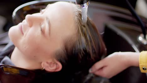 Hands-of-caucasian-female-hairdresser-washing-hair-of-relaxed-female-customer-at-hair-salon