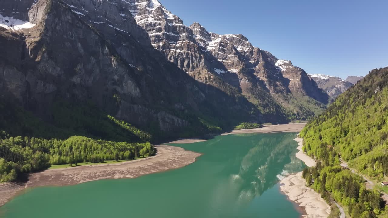 The glacier-carved valley holds the turquoise Klöntalersee in Schweiz, overlooked by sheer, snow-dusted Alpine peaks. Concept of glacial-fed tranquility and awe