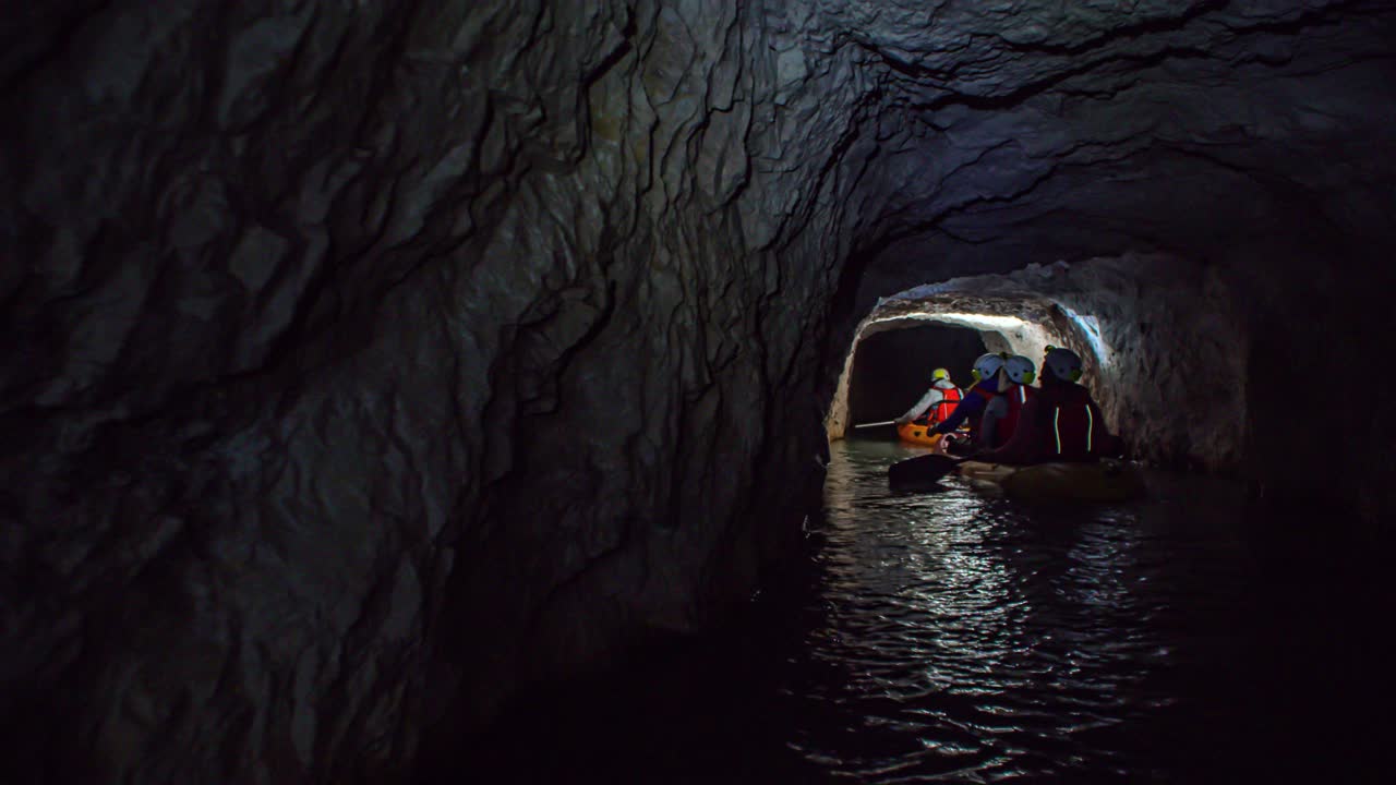 A follow shot of a group of people entering a dark cave by boats