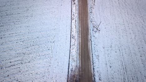 Drone-Flying-Over-Dirt-Road-Between-Snowy-Fields-In-Latvia,-Europe