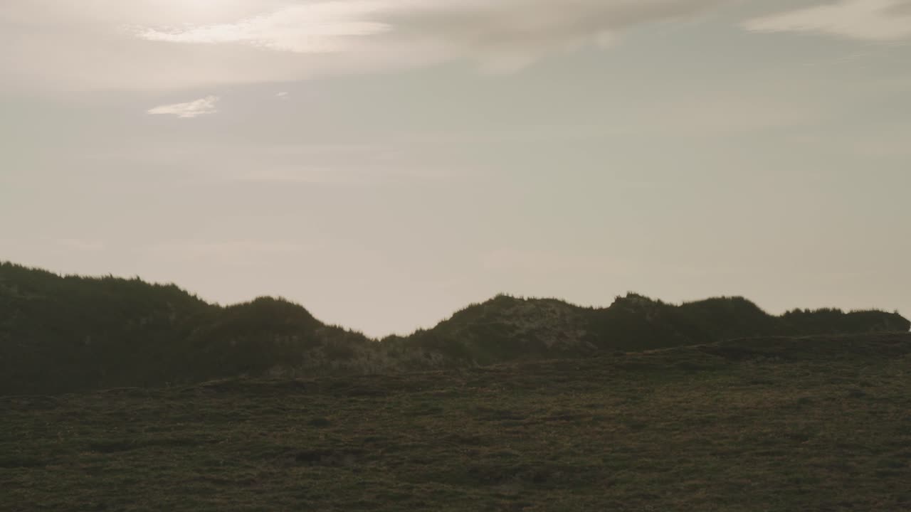 un paisaje sereno de dunas de hierba bajo un cielo nublado durante la puesta de sol