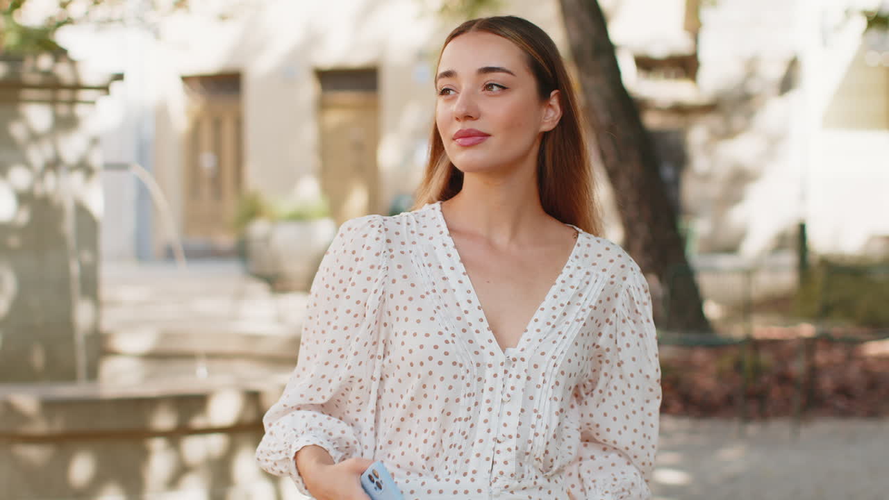 Giovane donna caucasica che usa lo smartphone, scrive messaggi sui social media, invia e-mail in una strada della città.
