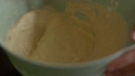 Person-stirring-pizza-batter-in-a-green-bowl-using-a-spoon