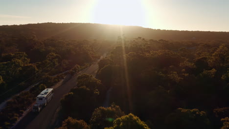 Aerial-shot,-Caravan-is-traveling-towards-sunrise-in-a-natural-landscape-in-the-forest