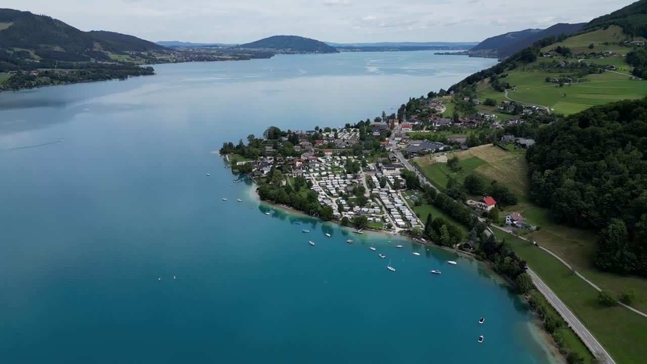 Cinematic drone shots capture Attersee’s crystal-clear waters, with charming lakeside homes nestled along the shores, surrounded by Austria’s lush, picturesque natural beauty.