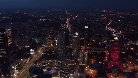 Slide-and-pan-shot-of-city-at-night.-Aerial-panoramic-footage-with-Zlote-Tarasy-shopping-mall-and-Palace-of-Culture-and-Science.-Warsaw,-Poland