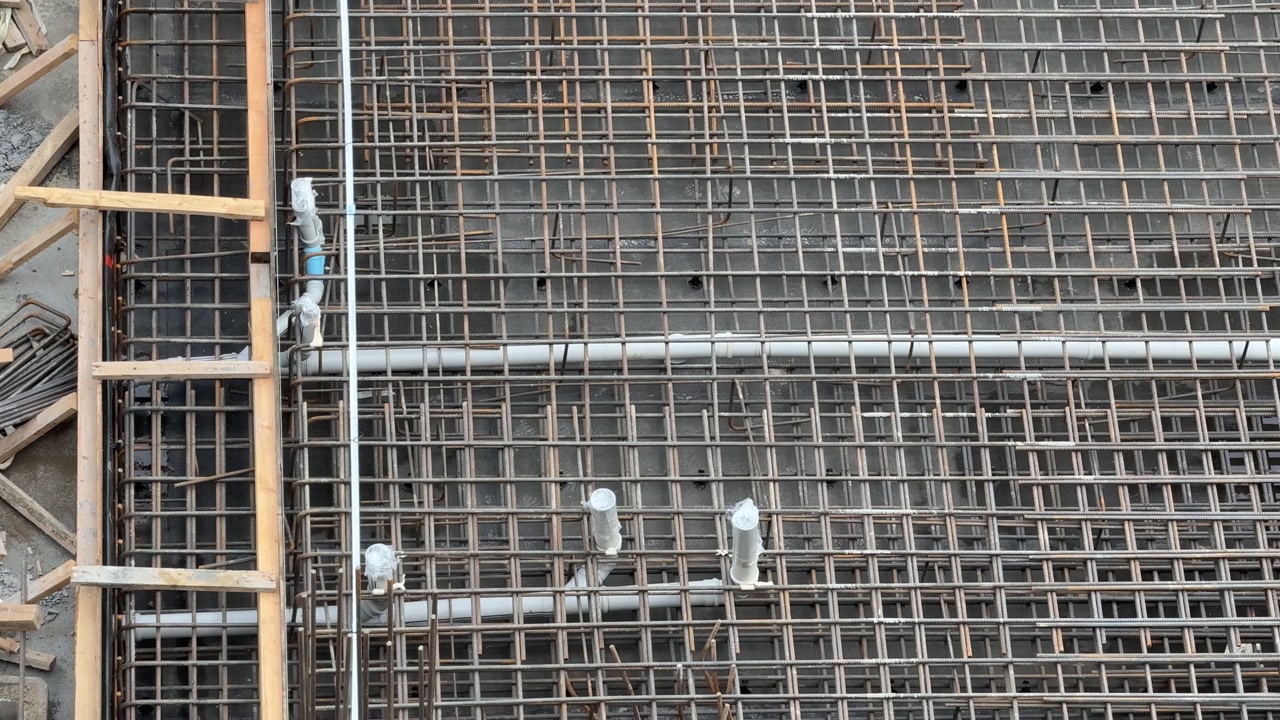 Close-up of densely woven steel reinforcement (rebar) and electrical or plumbing conduits running through the bars for a wall or slab of a concrete structure under construction. This structural prepar
