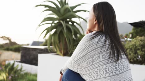 retrato de una mujer biracial sonriente sentada y admirando la vista en el jardín, en cámara lenta
