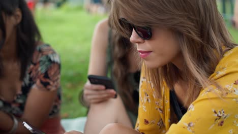 Mujer-Sonriente-Sentada-En-El-Césped-Y-Usando-Un-Teléfono-Móvil.