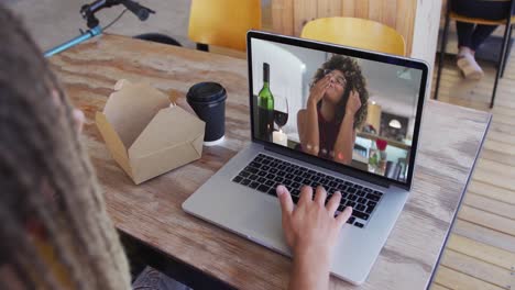 hombre de raza mixta sentado en una cafetería usando una computadora portátil haciendo una videollamada con una amiga