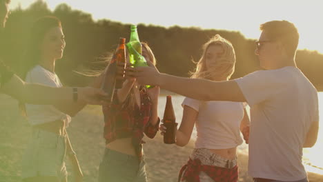 five students celebrate a birthday on the open air party with beer and good mood. they drink beer and dance in the summer evening near the lake coast. this is carefree party at sunset.