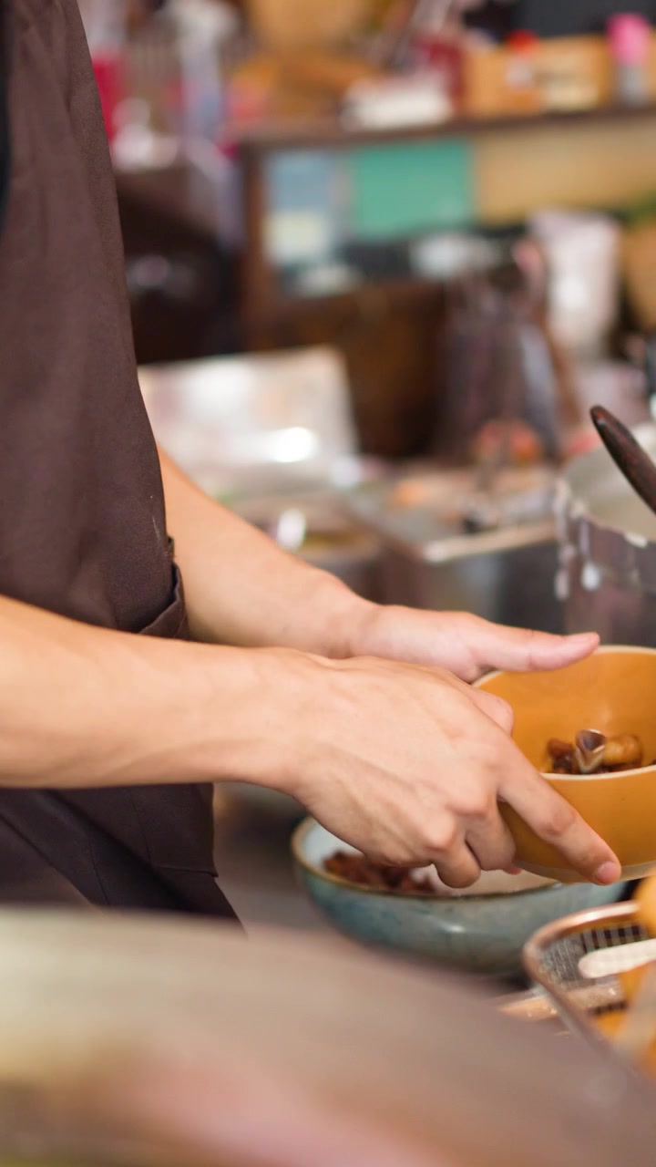 Close-up of vendor hands using ladle to serve hot soup into bowls at market.