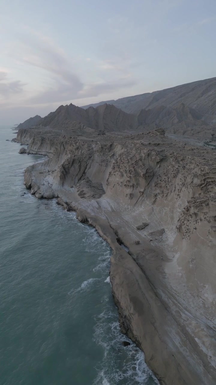 Montagne e oceano vicino all'ambiente di erosione delle scogliere e paesaggio di forme terrestri marziane con picchi, spiagge, mare, yardang e lucidatura eolica in Iran, avventura aerea al tramonto panoramico sulla costa dell'Oman con il golfo all'orizzonte.