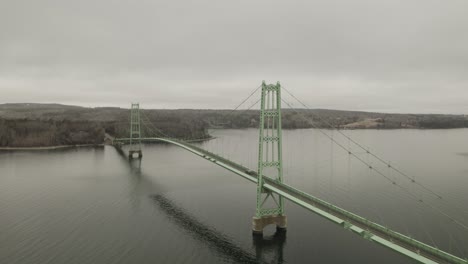 Drone-shot-of-a-green-bridge-on-a-cloudy-day,-with-one-car-driving-over-it,-panning-to-the-right