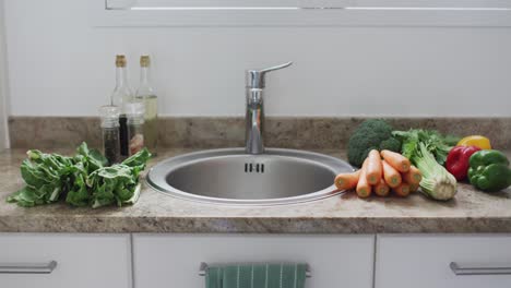 fresh organic vegetables sitting on worktop by kitchen sink, ready for washing