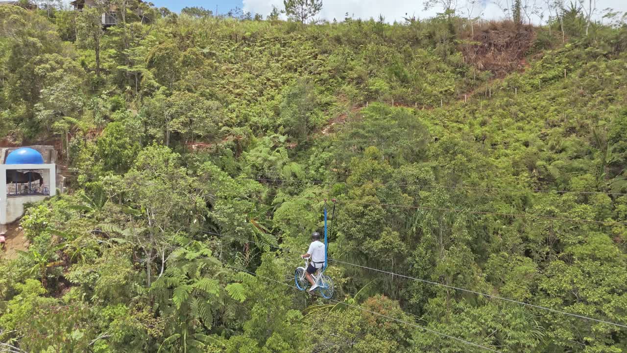 Cinematic 4K drone footage of a tourist riding a sky bike suspended above dense jungle toward an adventure station in the Philippines, ideal for travel, adventure, and eco-tourism projects