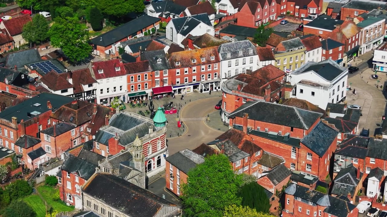 Luftoptagelser med drone af Romseys bymidte i Hampshire, der viser hovedgaden, historiske bygninger, hustage, butikker, veje, fodgængere og lokal arkitektur på en solrig dag. Relevant for britiske formål.