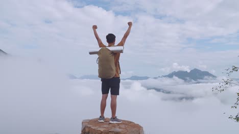 asian hiker male standing on the rock and raising his hands celebrating reaching up top of foggy mountain