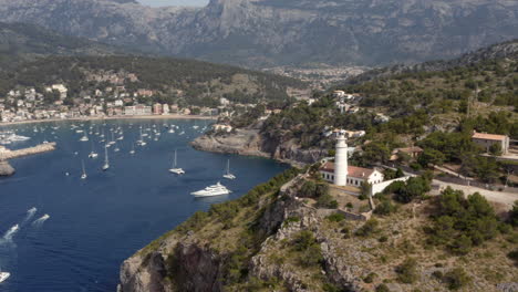 white lighthouse above bay in port de sóller town with anchoring boats