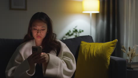 woman sitting on a couch at night using her phone