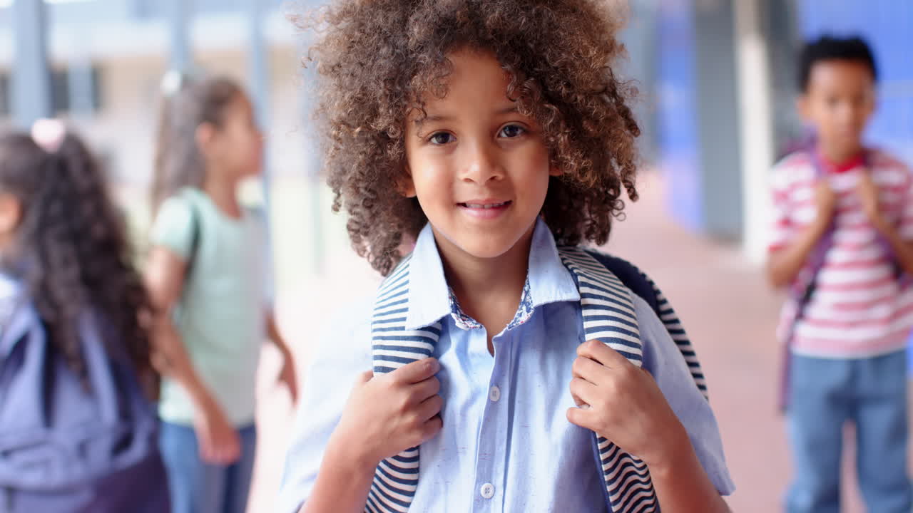 Smiling boy holding backpack, standing in school hallway with classmates