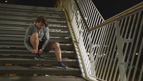 Hombre-Caucásico-Sonriendo-Y-Atando-Su-Encaje-En-Las-Escaleras-Por-La-Noche