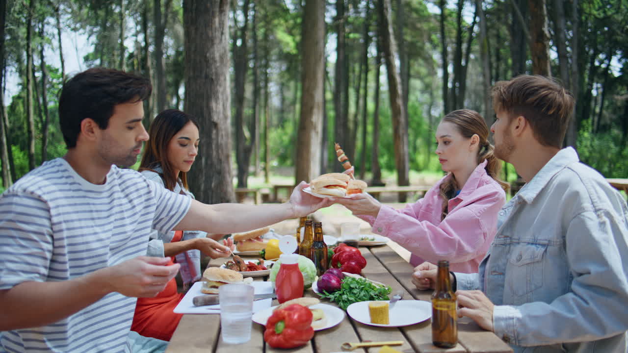 Friends enjoying picnic meal in sunny forest closeup. Women man sharing burgers