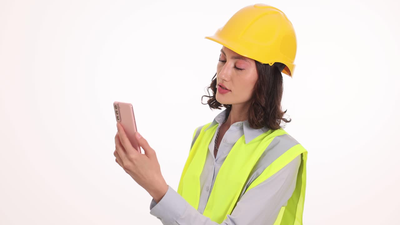 A woman engineer or construction worker in a hard hat and safety vest looking at her phone