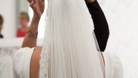 woman touching up bride's hair with veil in slow motion before wedding