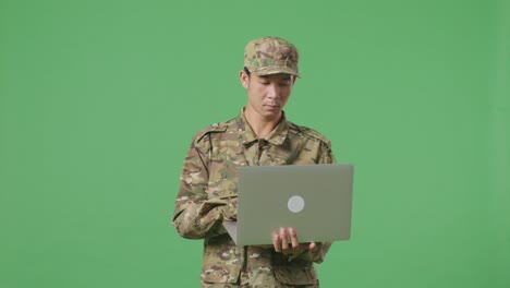 un soldado asiático usando una computadora portátil mientras camina en el estudio de fondo de la pantalla verde
