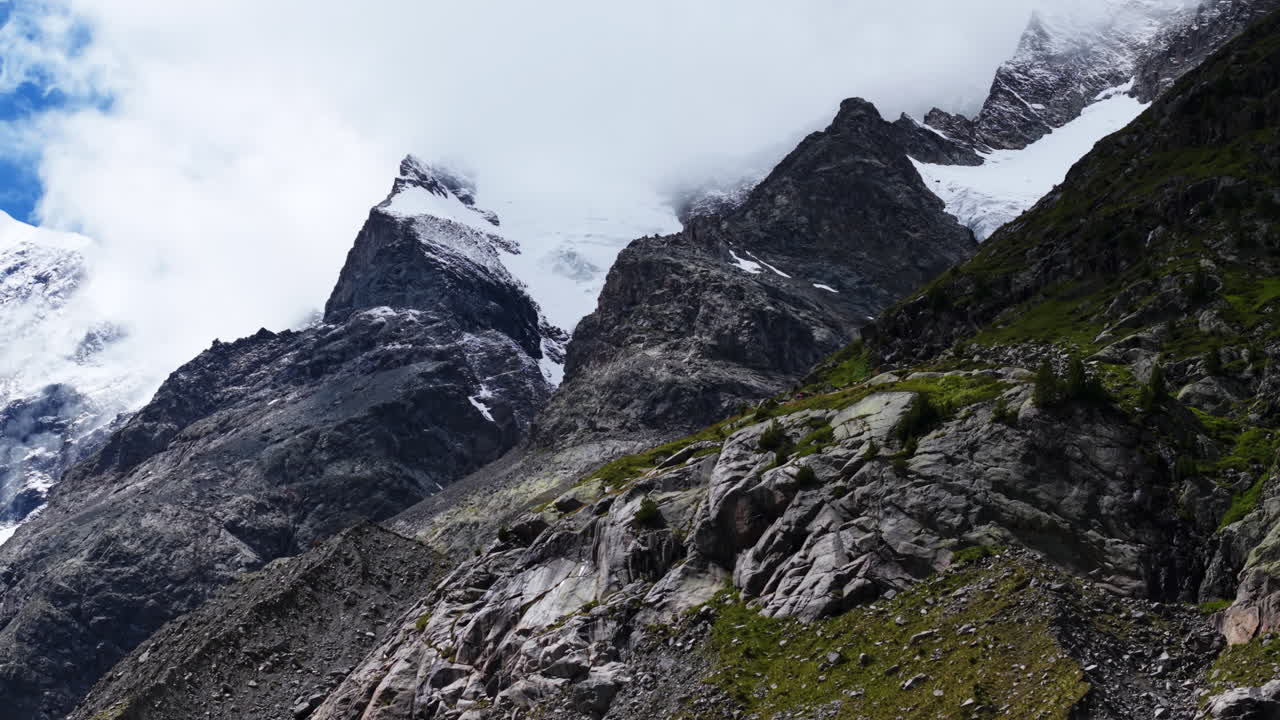 Drone ascends mountain slope revealing snowy peaks lost in clouds