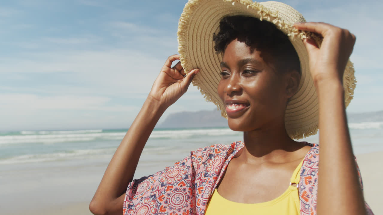 Ritratto di donna afroamericana felice con cappello su una spiaggia assolata