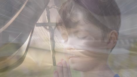 animation of light spots over caucasian boy praying and cross