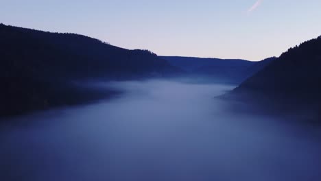 beautiful dark aerial drone fly at sunset over a sea of fog in a mountain valley with orange sky