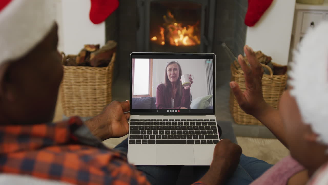 Coppia afroamericana con cappelli di Babbo Natale che usa un laptop per una videochiamata di Natale con una donna sullo schermo